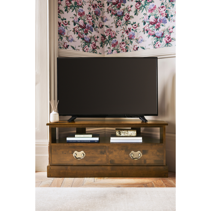 Wooden TV stand with a television and decor in a room with floral wallpaper.