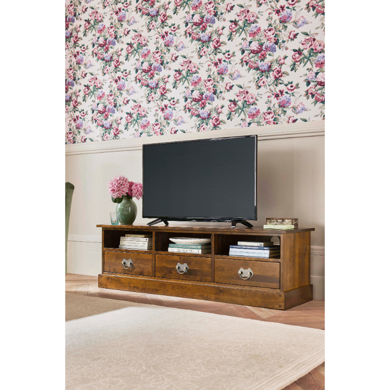 Wooden TV stand with a television and floral decor in a room with floral wallpaper.