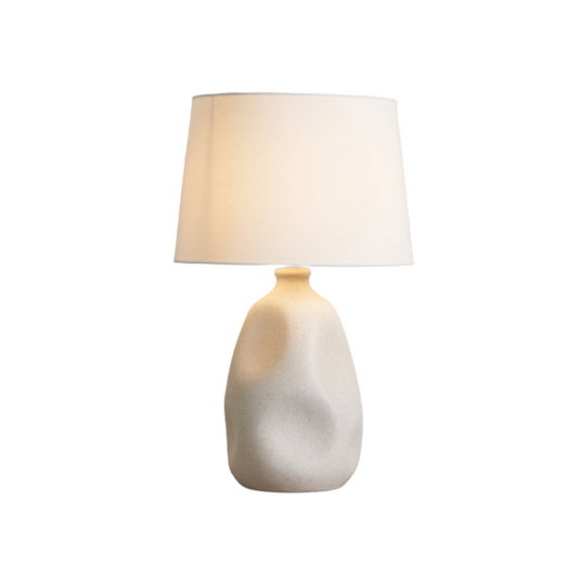 Table lamp with a textured ceramic base and white shade on a white background