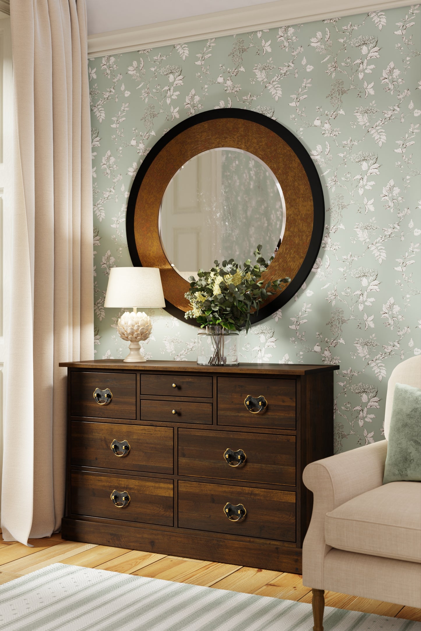 Wooden dresser with round mirror and floral decorations in a room with floral wallpaper.