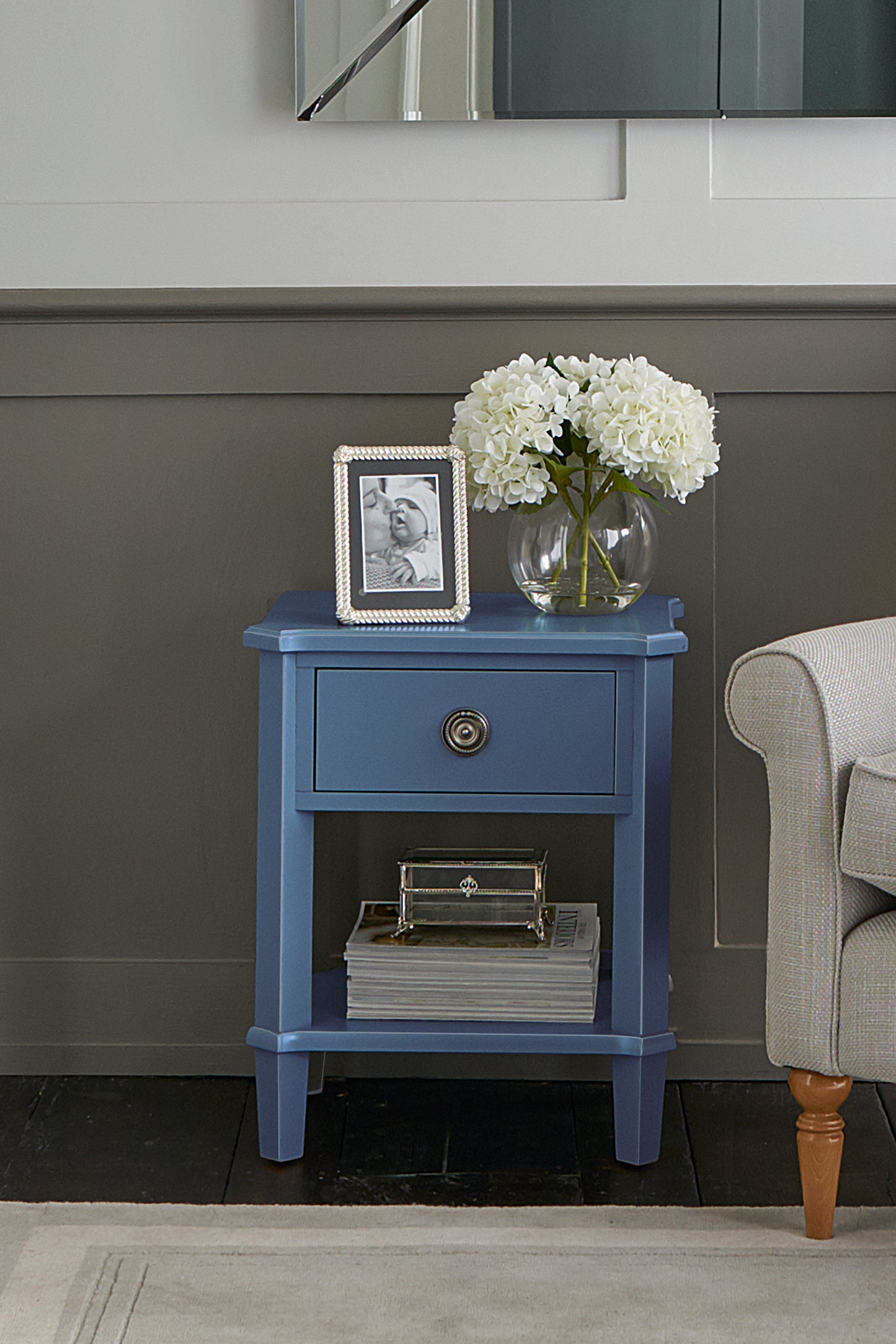 Blue side table with a vase of flowers and photo frame against a gray wall.