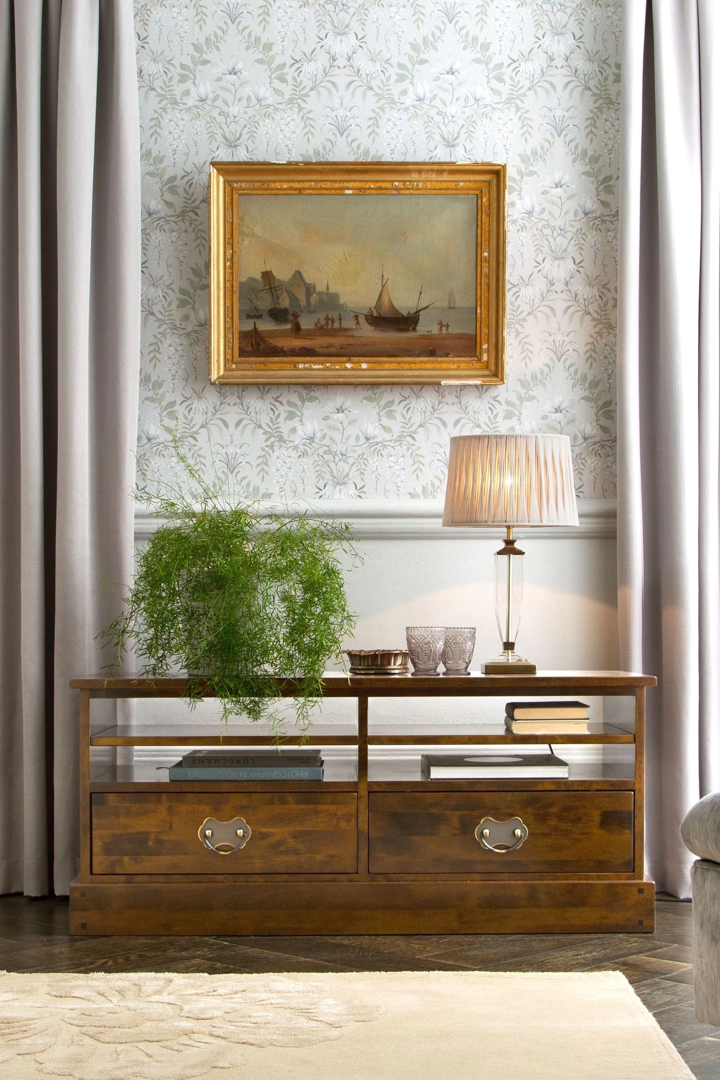 Wooden console table with lamp and plant against decorative wall paper.