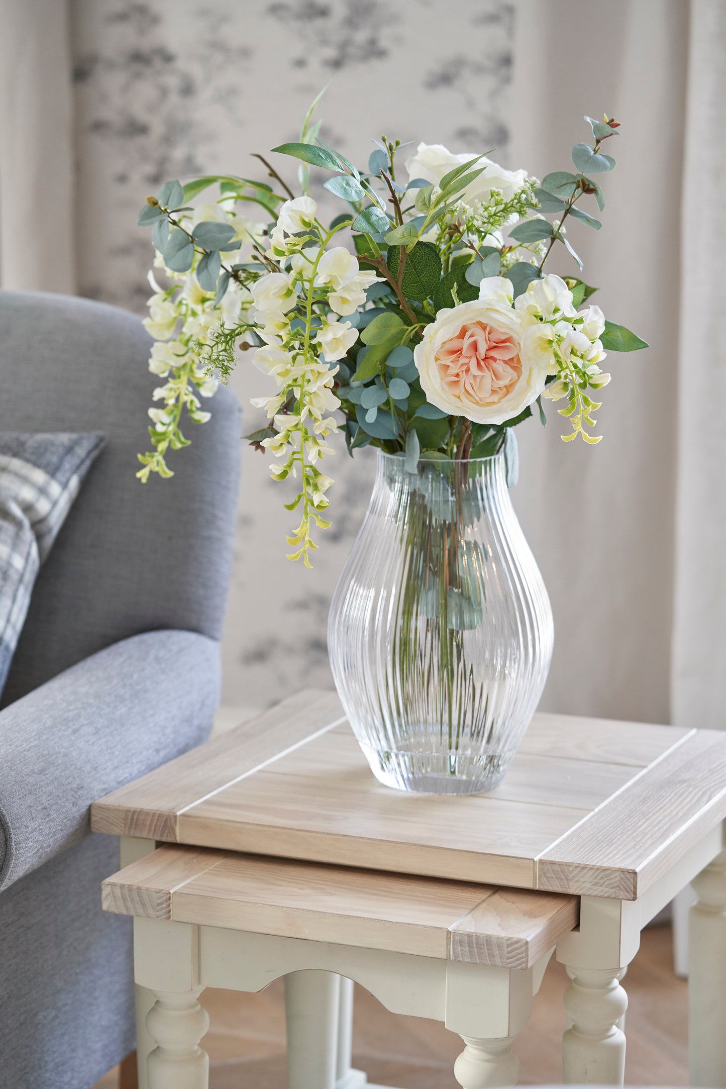 A white and brown nest of two tables with a wooden top and carved legs. A vase of flowers stands on top