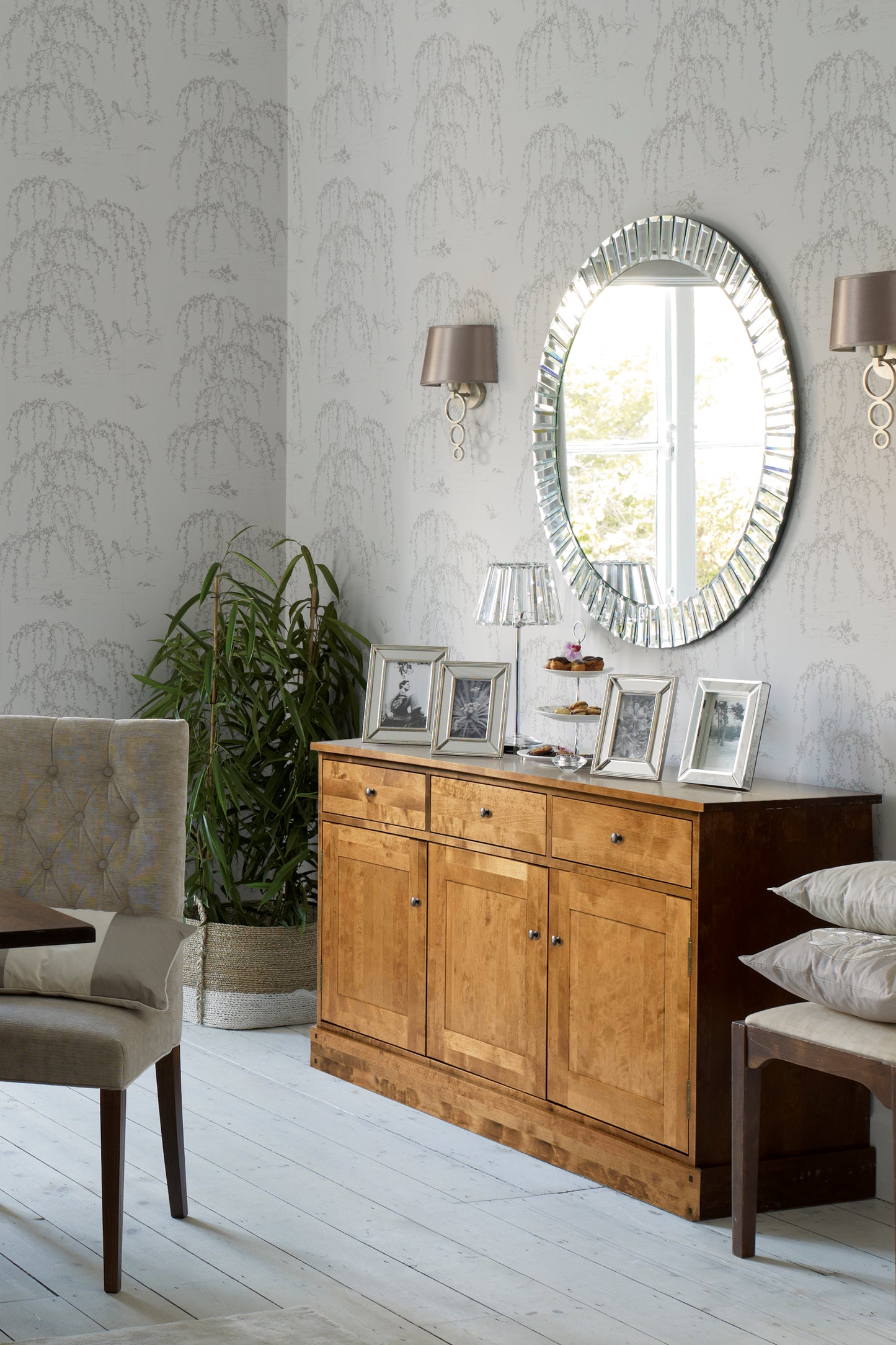 Room with wooden honey-coloured sideboard with three doors and three drawers, mirror, and chairs.