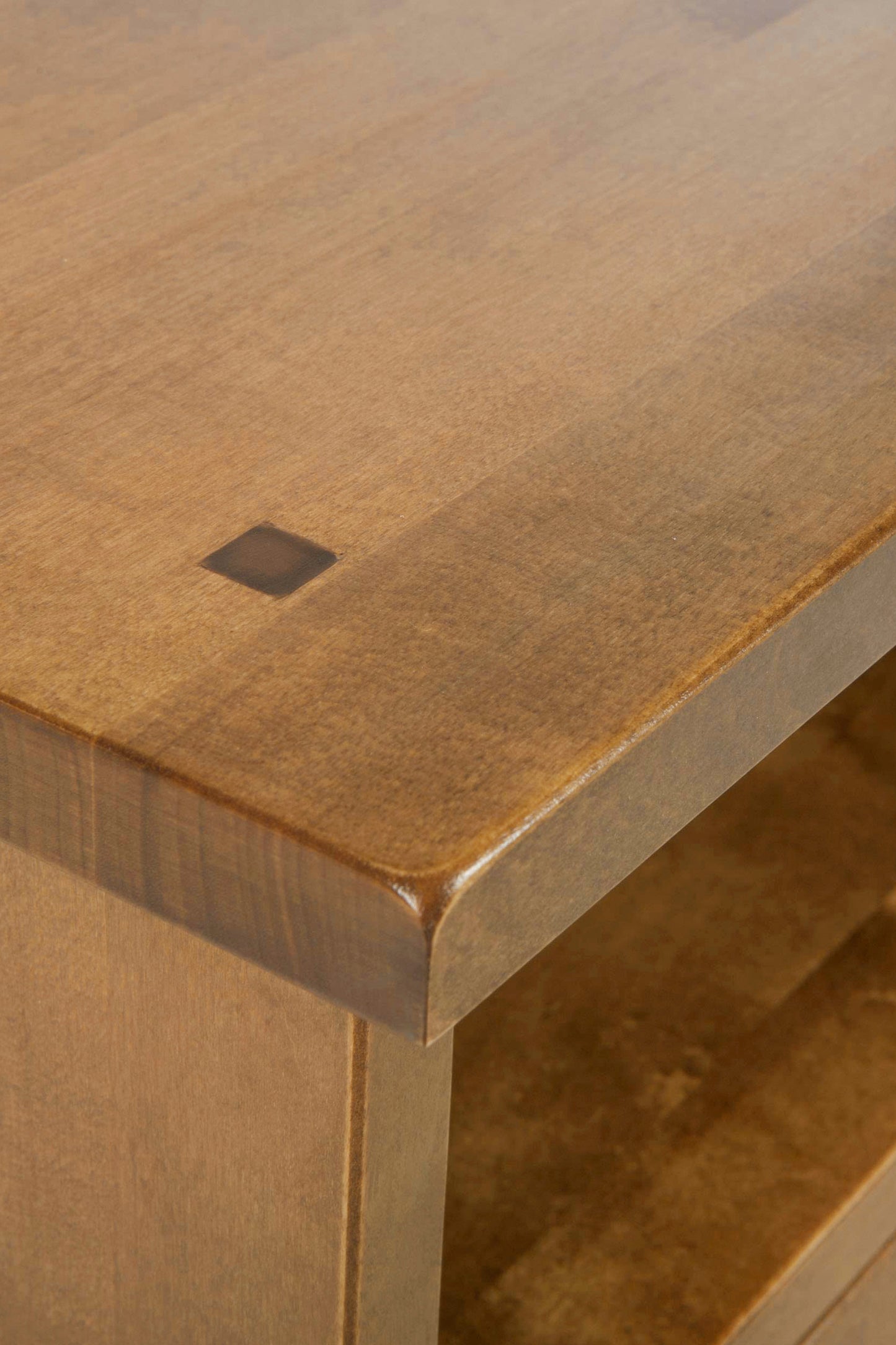 Close-up of a wooden table surface with a small square hole.