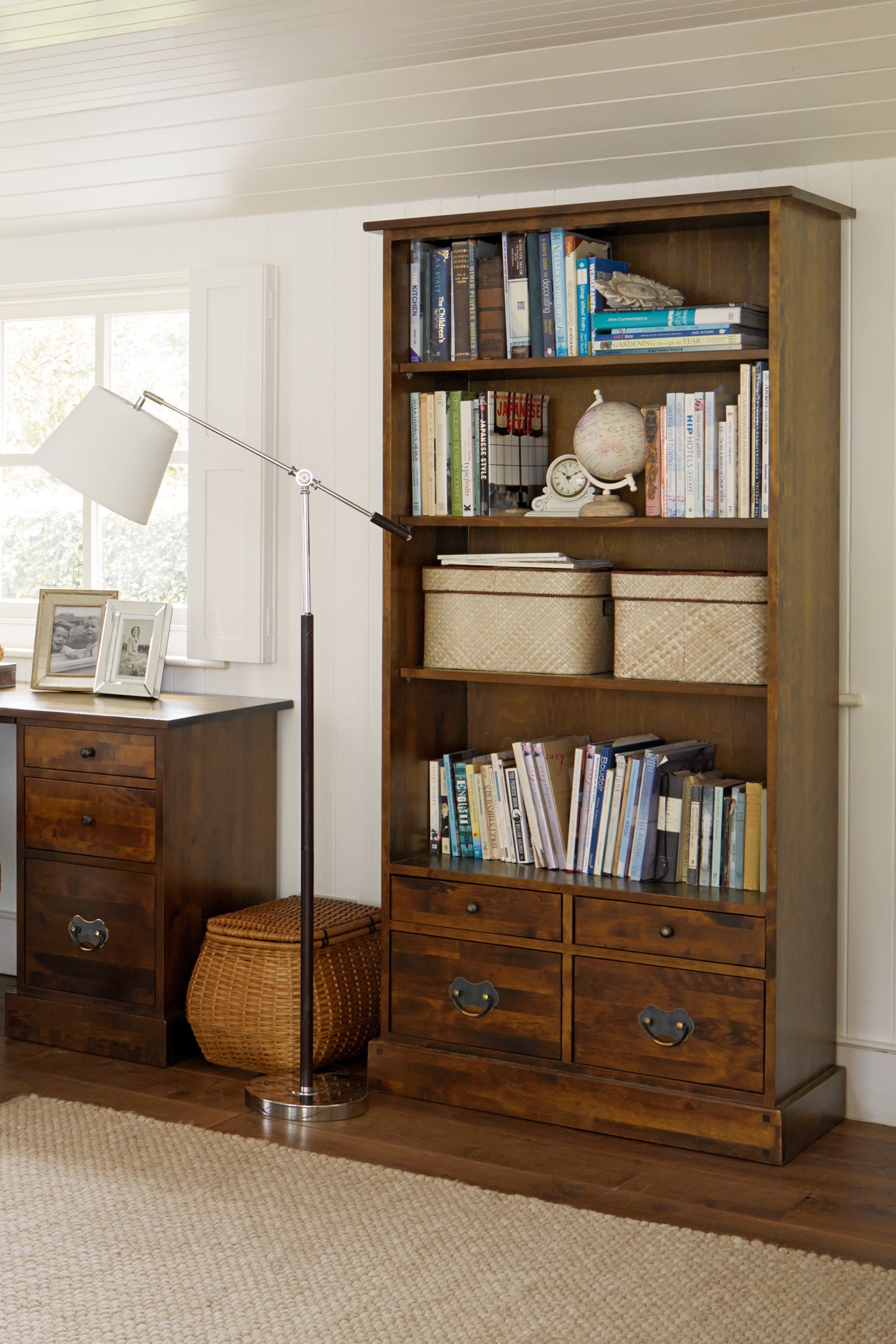A dark chestnut wooden bookcase with four shelves and four drawers displaying books and decor in a room setting