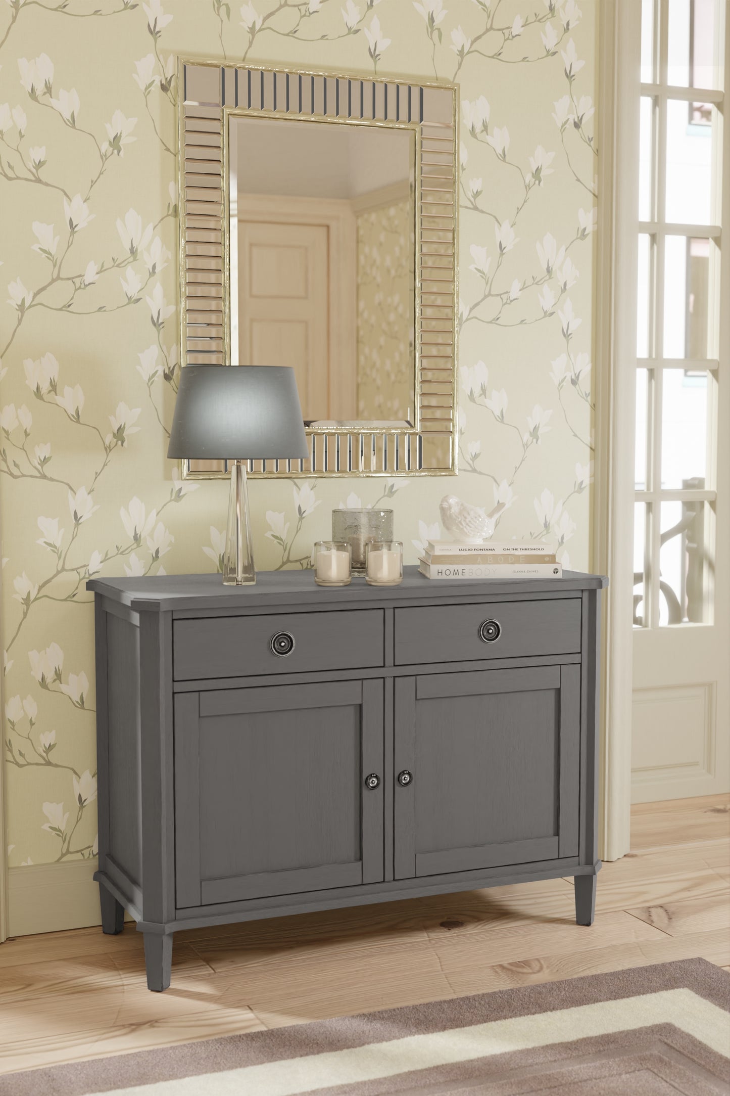 Gray bathroom vanity with mirror and decorative items against floral wallpaper.