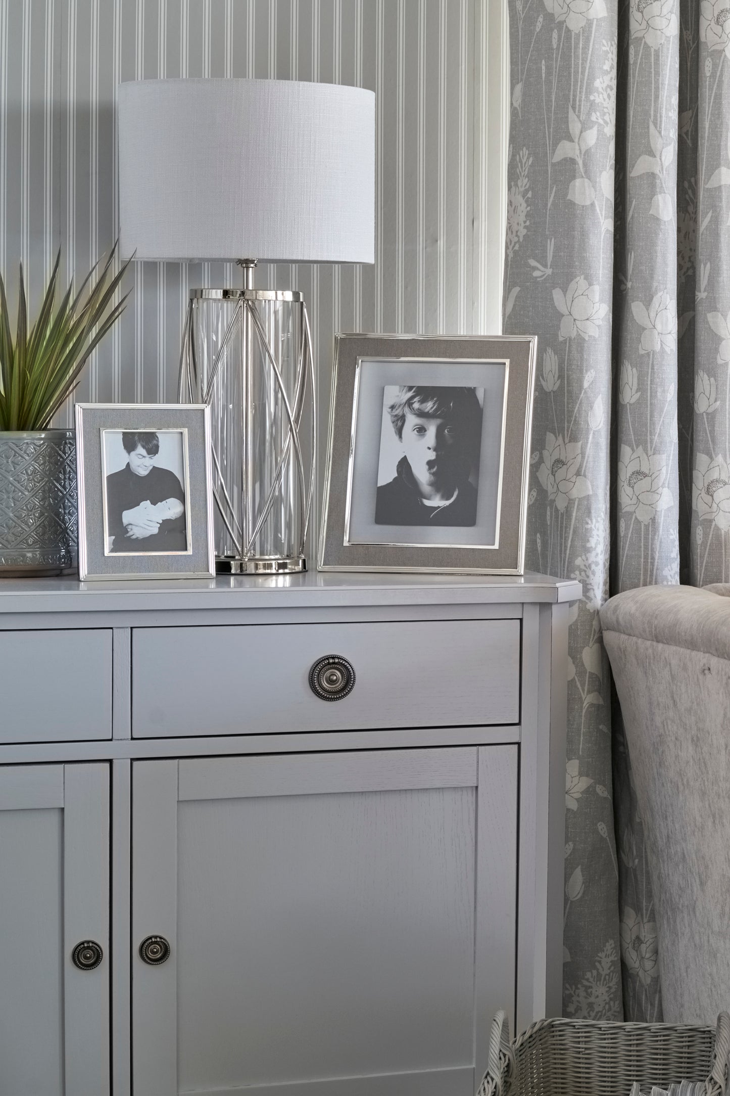 Gray cabinet with framed photos and a lamp against a floral curtain background