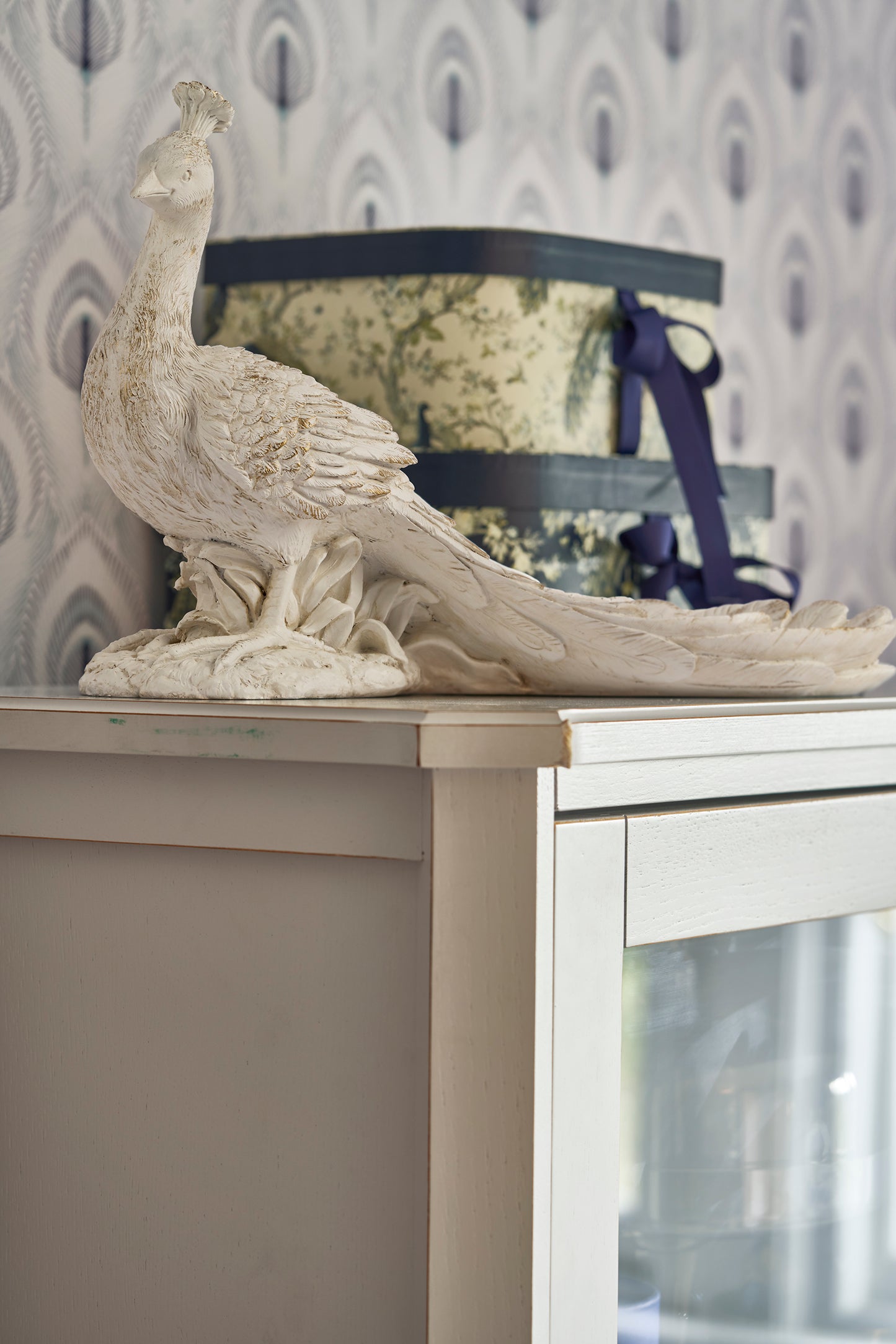 Decorative peacock statue on a surface with a patterned wallpaper background