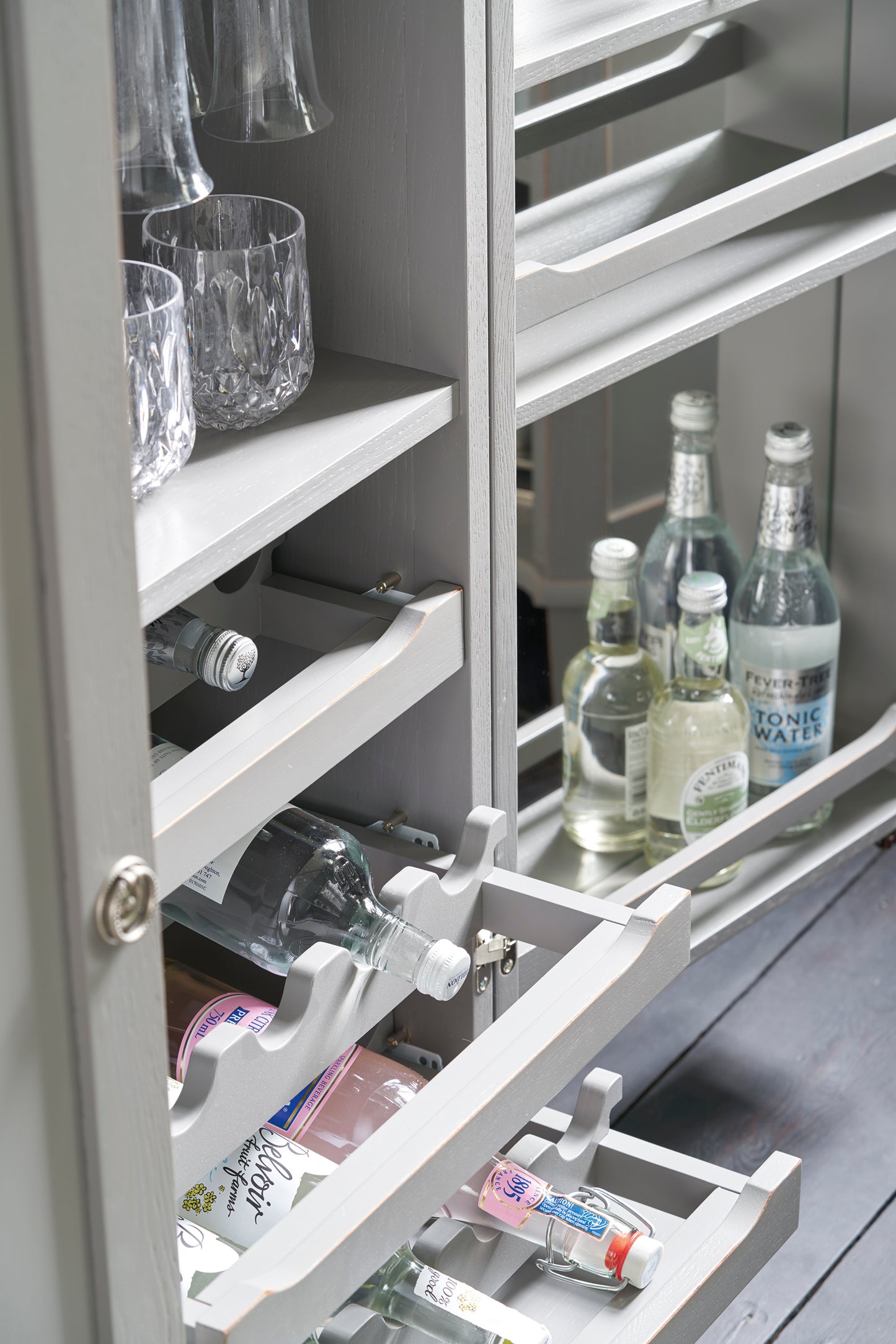 Grey drinks cabinet with open shelves containing bottles and glasses