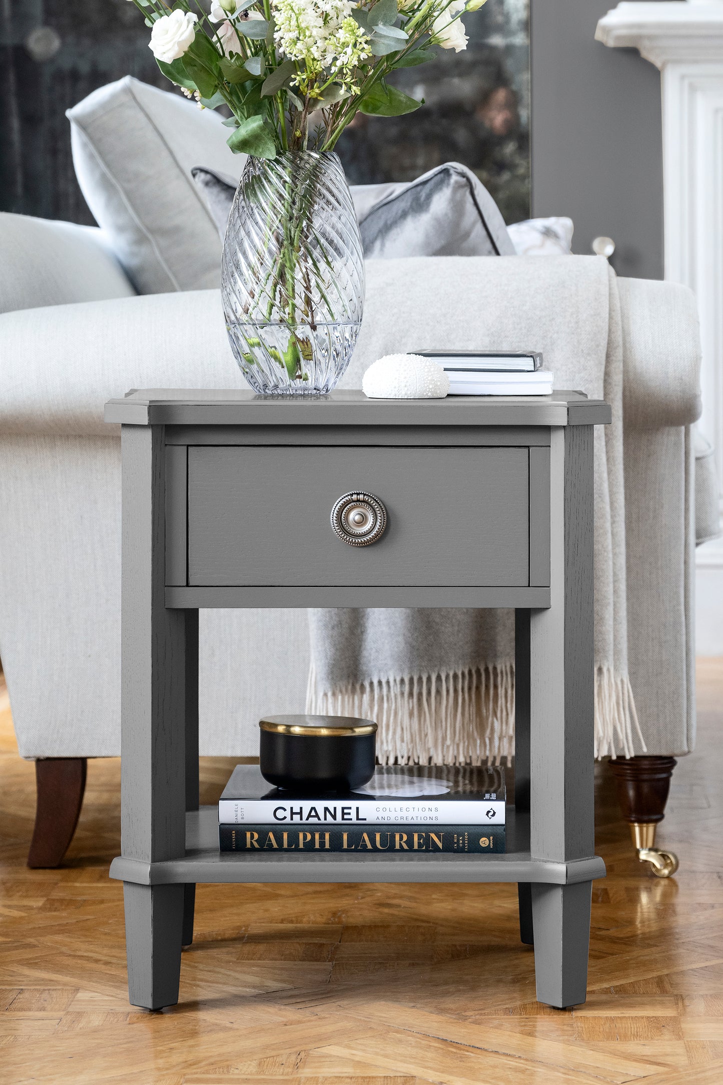 Gray side table with a vase of flowers, books, and a bowl in a living room setting.