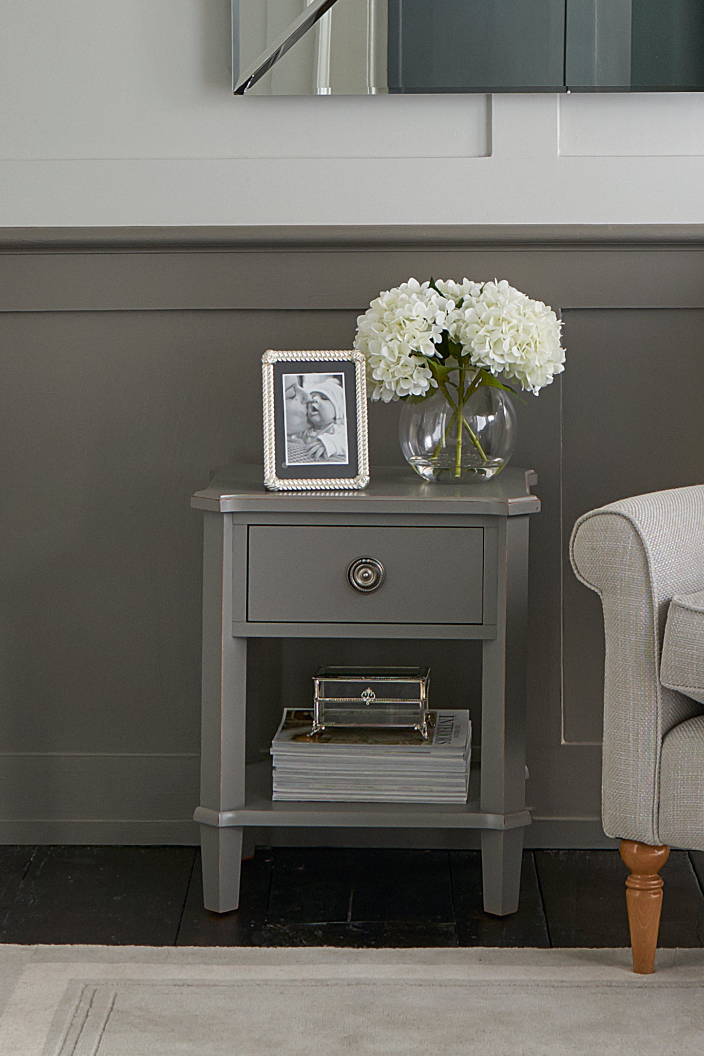 Gray side table with a vase of flowers and photo frame against a gray wall.