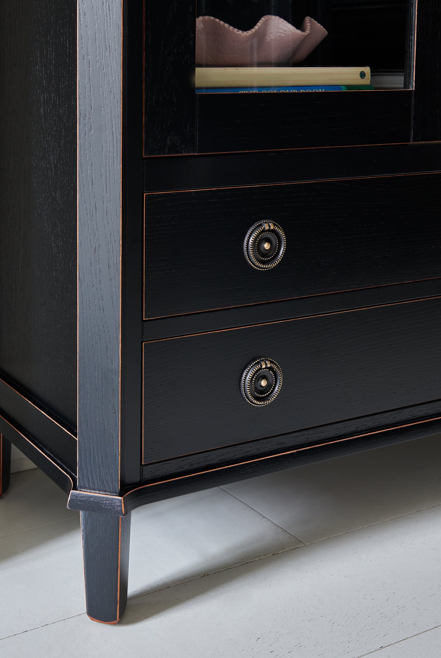 Close-up of a dark wooden dresser with brass knobs on a light gray floor.