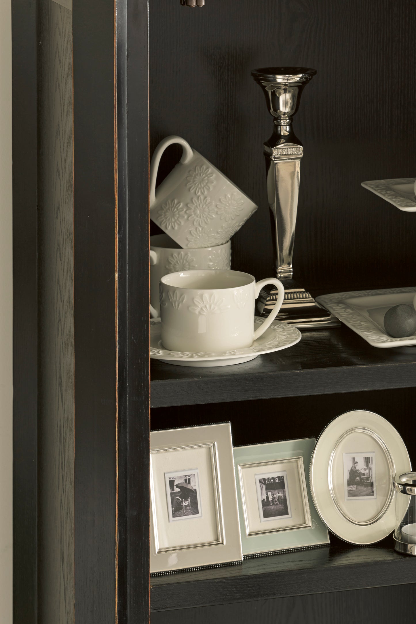 Decorative shelf with cups, plates, and framed pictures against a dark background