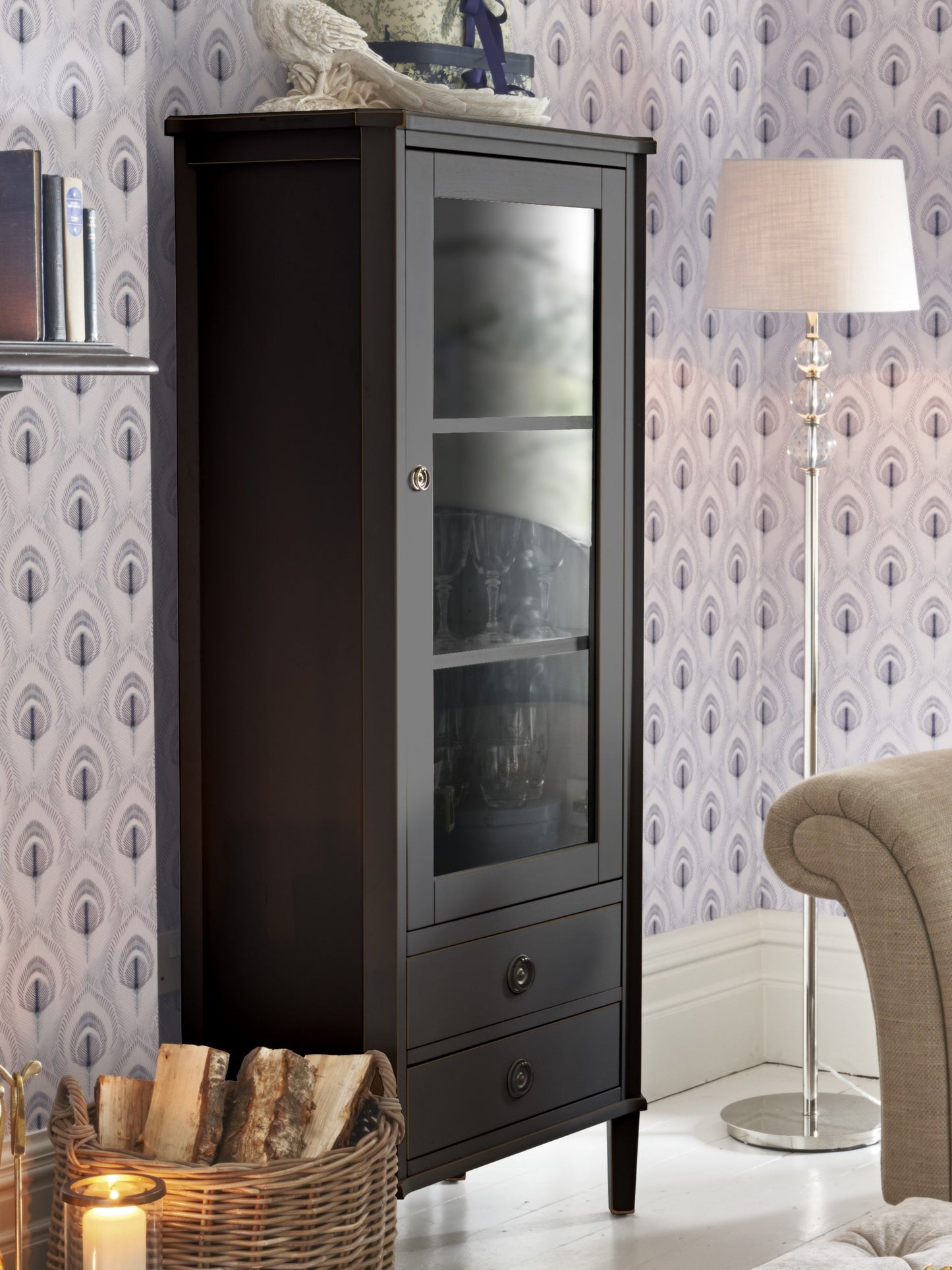 Dark wooden cabinet with glass doors in a room with patterned wallpaper and a lamp.