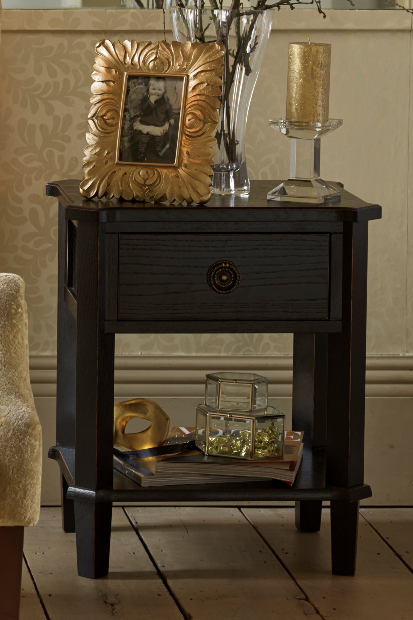 Dark wooden side table with gold frame, decorative items, and patterned wallpaper.