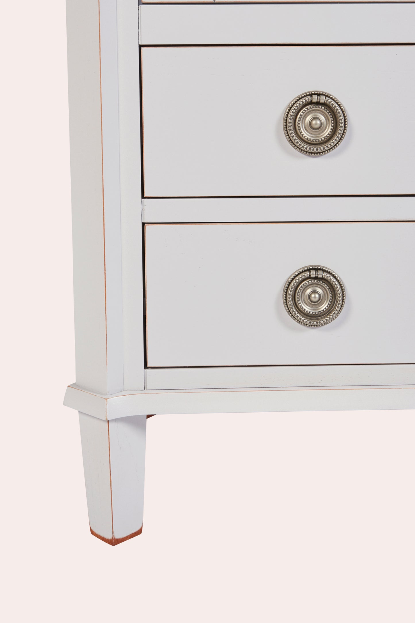 Close-up of a white dresser with decorative silver knobs on a light gray background