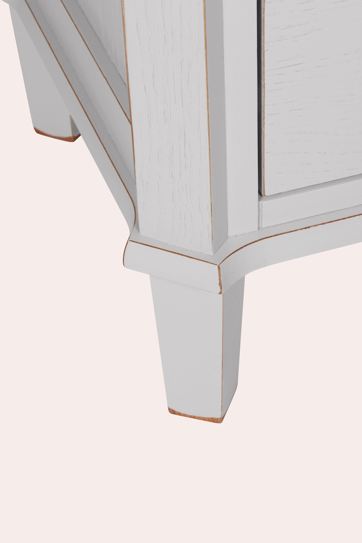 Close-up of a white wooden cabinet corner with a gold trim on a light pink background