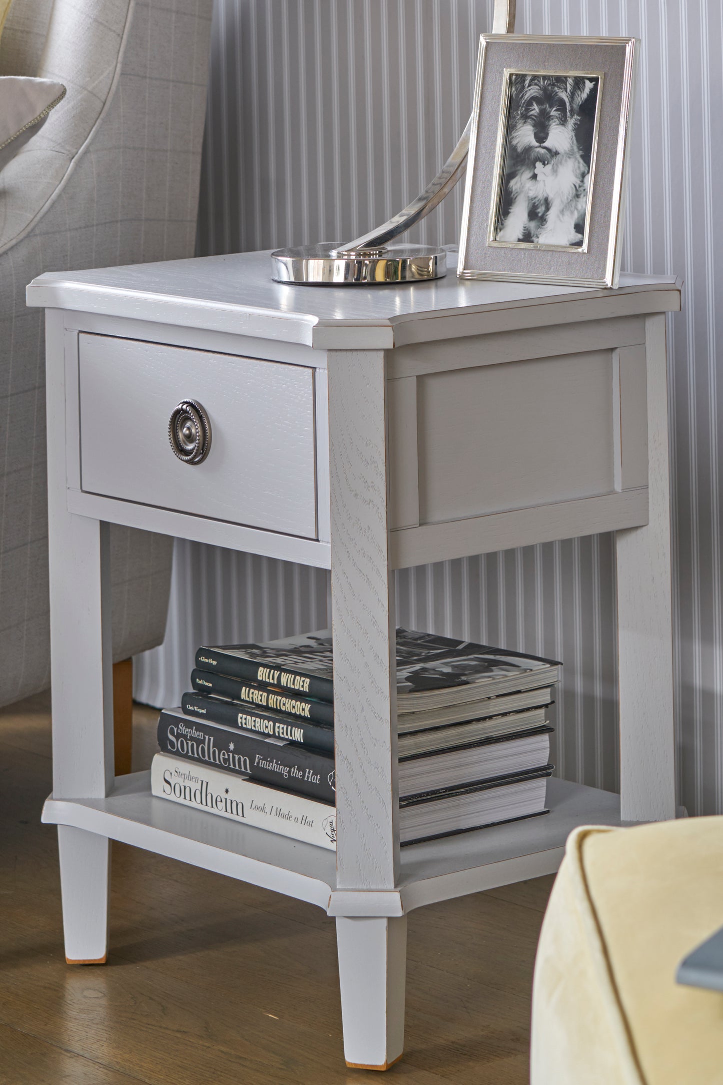 Gray side table with a drawer, books, and a framed picture on top.
