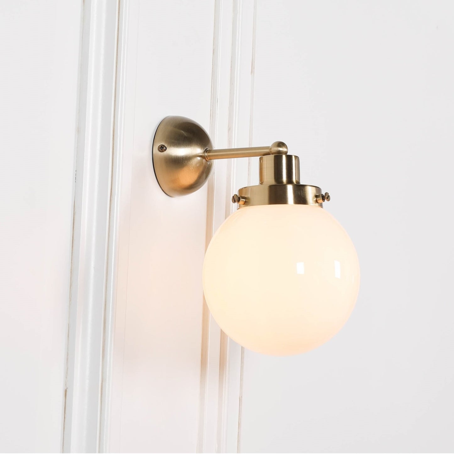 A brushed gold style brass wall light with a frosted glass globe, mounted on a white wall.