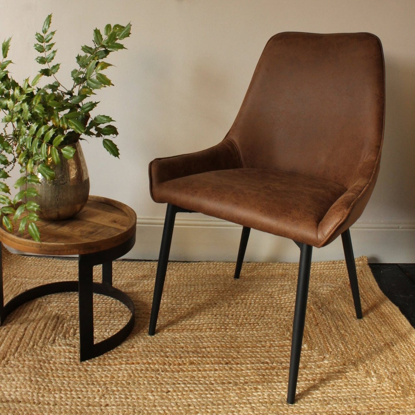 A brown vegan leather dining chair with a metal leg, positioned in a room with a round wooden table and a potted plant.