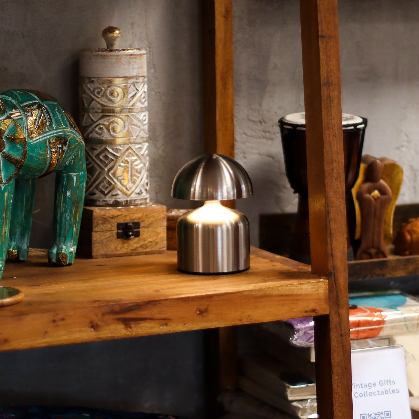 wooden Shelf with a silver metallic dome-shaped touch lamp surrounded by decorative items including a teal elephant and a textured cylindrical object.