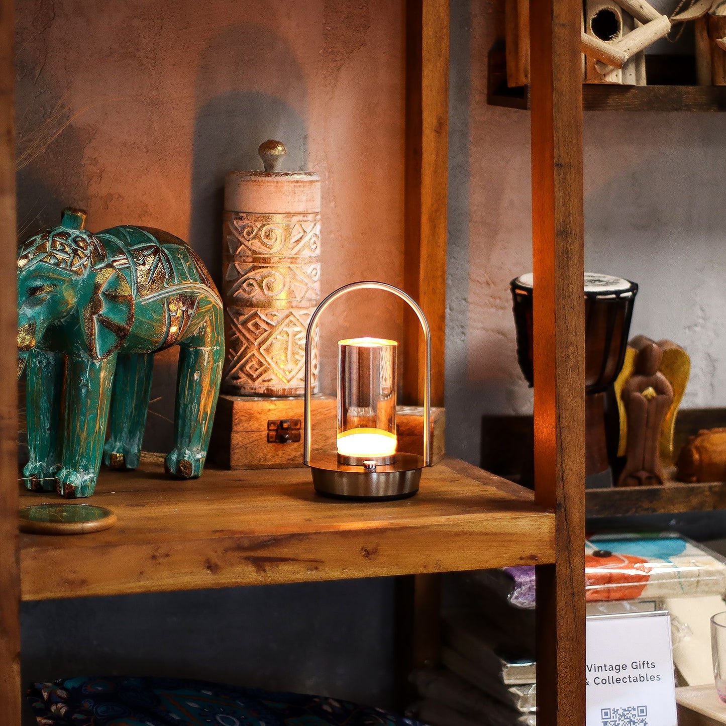 A lantern-style touch lamp surrounded by decorative items including a teal elephant figurine and a candle lantern on a wooden shelf.