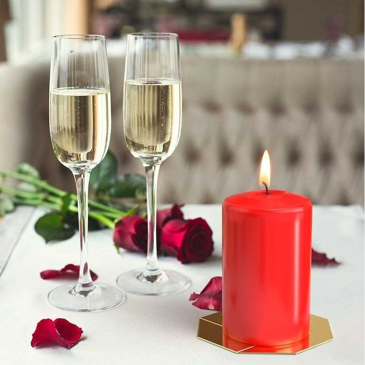 Two champagne glasses with a red candle on a table with flowers in the background