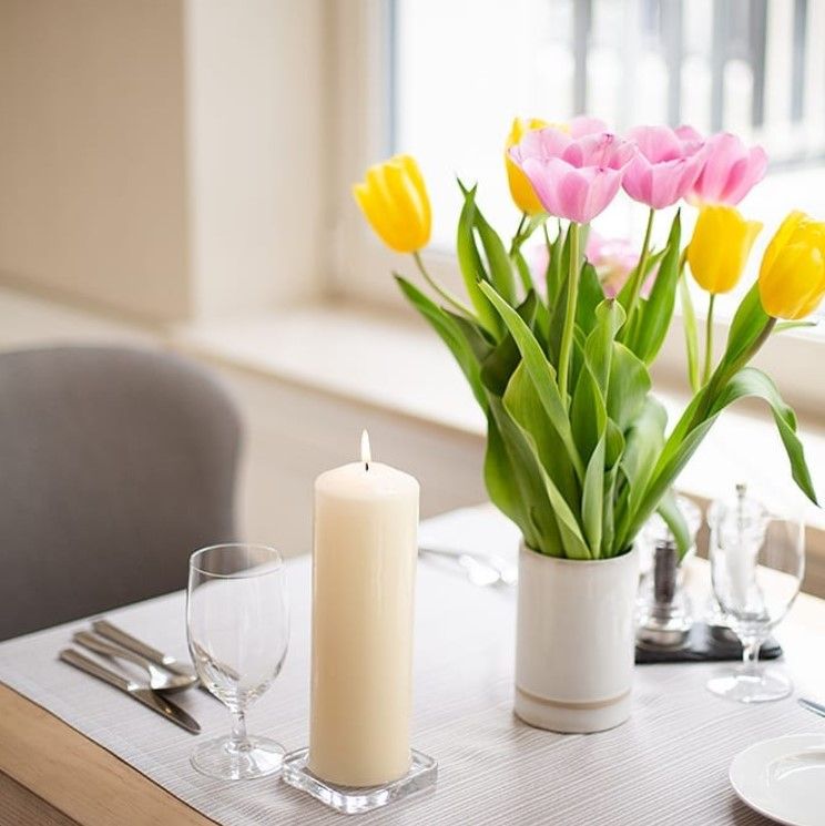 Table setting with tulips in a vase, candle, and glasses.