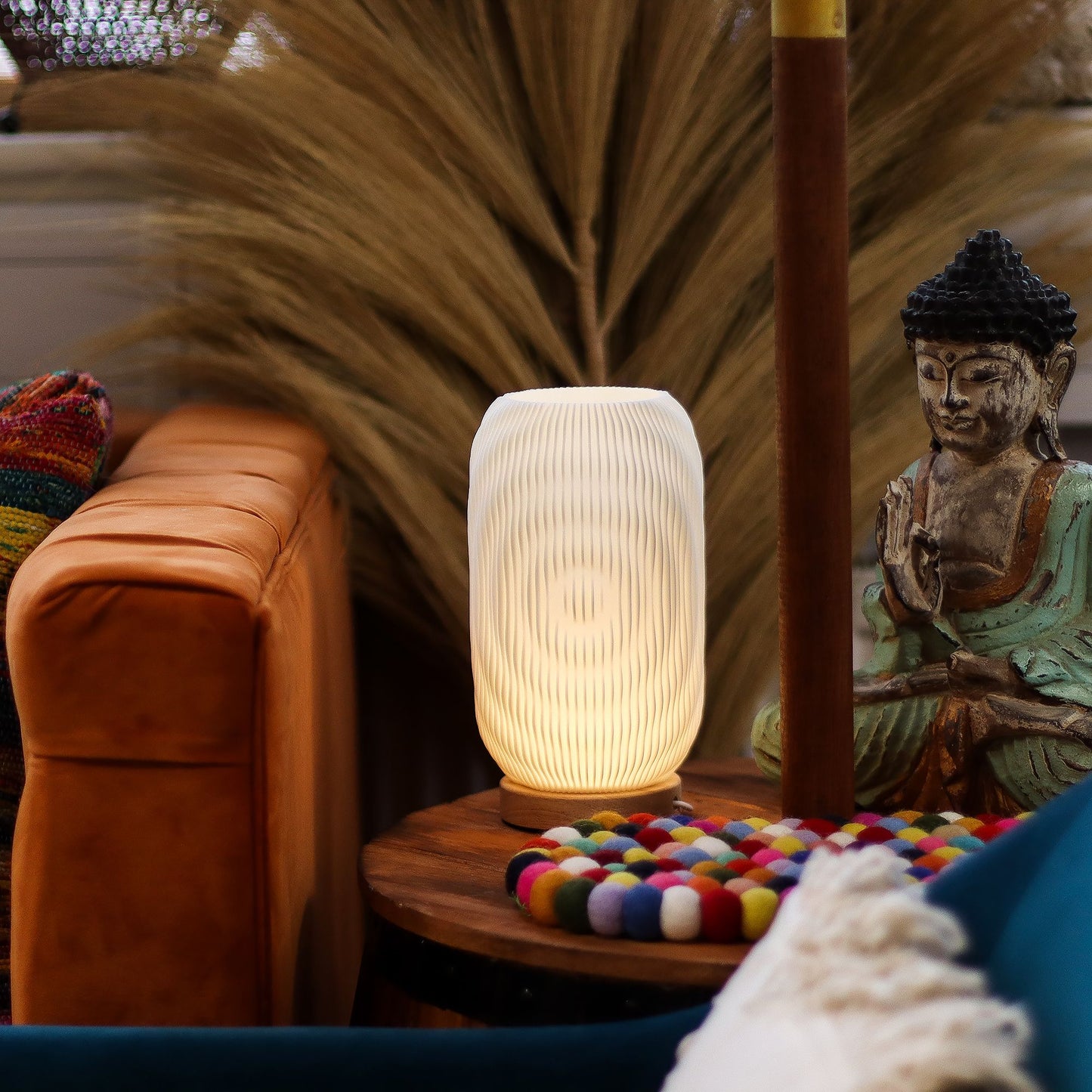 Decorative lamp on a table with a Buddha statue and colorful items in a cozy room setting.