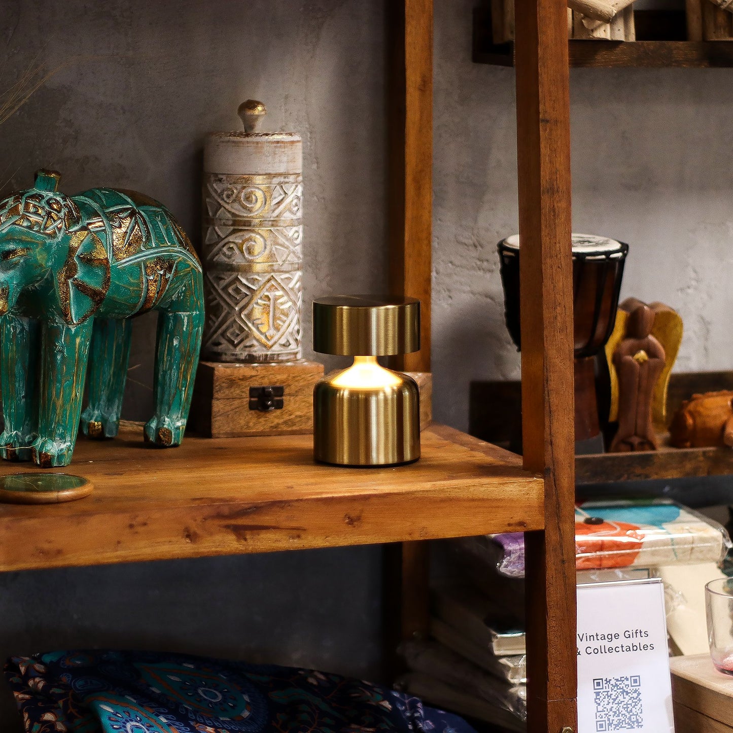 Gold touch lamp on a wooden shelf surrounded by other vintage-style decor items including a teal elephant, gold lamp, and other collectibles.