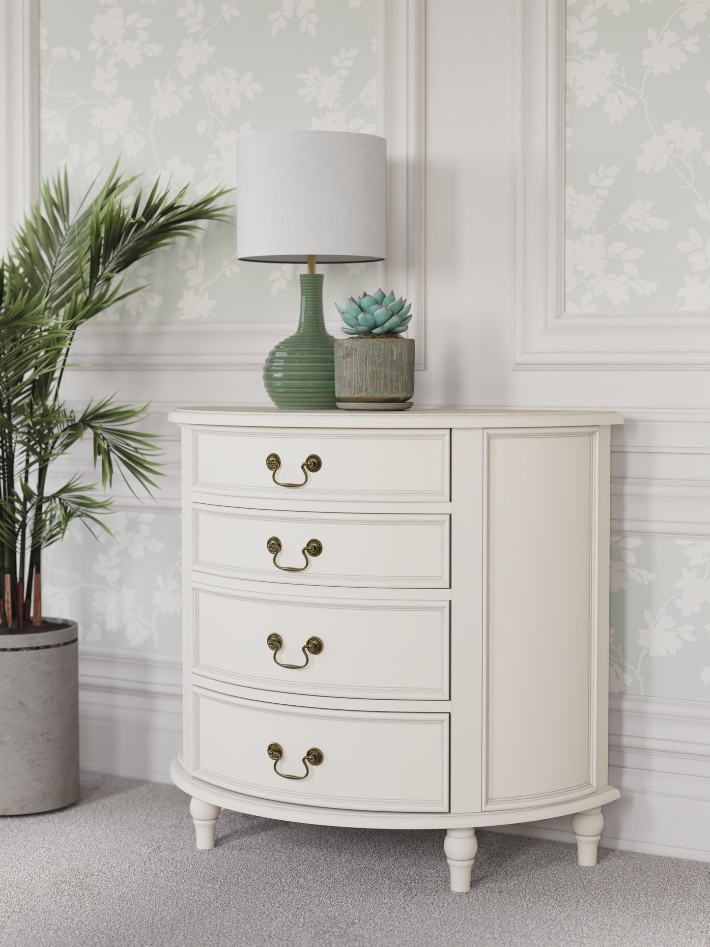 A left-hand corner view of an Ivory coloured half moon chest with four drawers and vintage styling. A lamp and some plants are shown with it