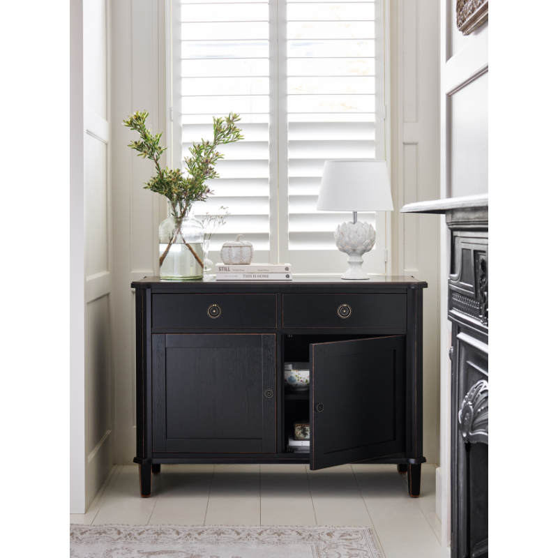 Black sideboard with open door in a room with a window and decorative items.