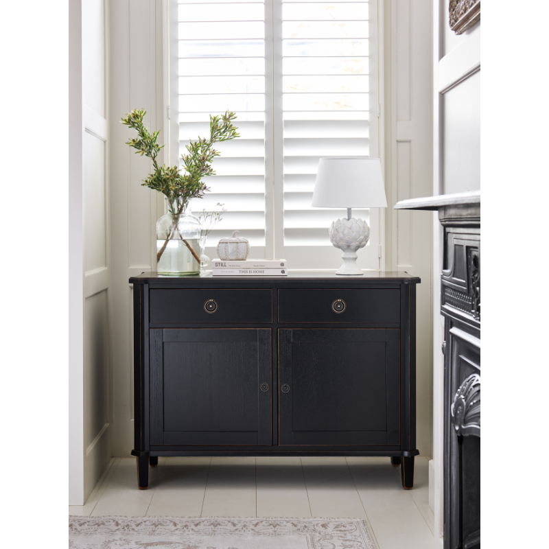 Black cabinet with decorative items in a room with a window and fireplace.