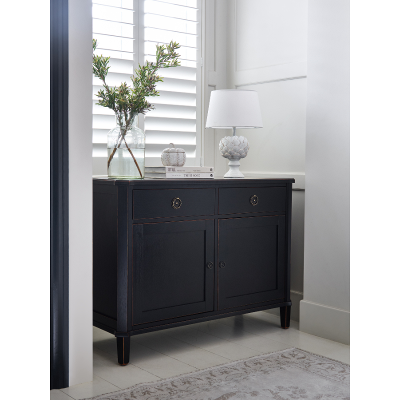 Dark wood sideboard with decorative items in a room with white walls and a window.