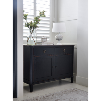 Dark wood sideboard with decorative items in a room with white walls and a window.