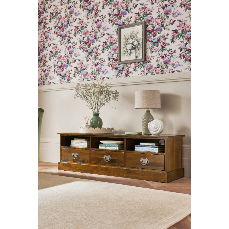 Wooden TV stand with decorative items against floral wallpaper.
