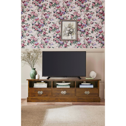 Wooden 3 drawer TV stand with a television and decor in a room with floral wallpaper.