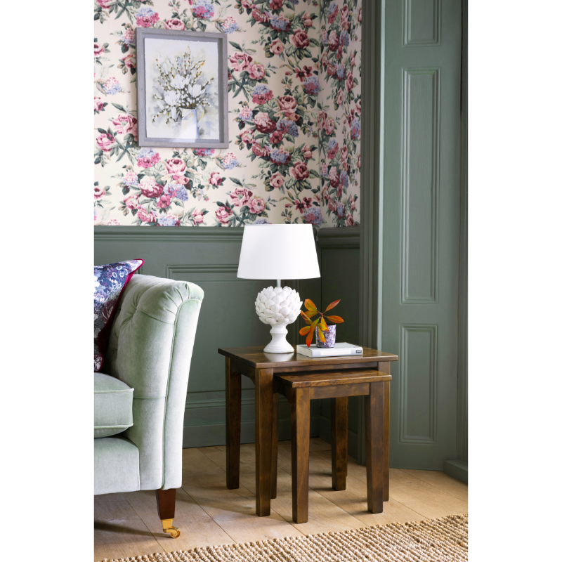 Cozy corner of a room with floral wallpaper and a lamp on a wooden set of 2 nesting table.