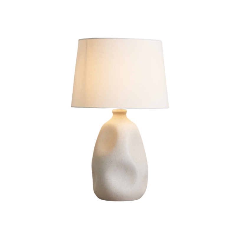 Table lamp with a textured ceramic base and white shade on a white background