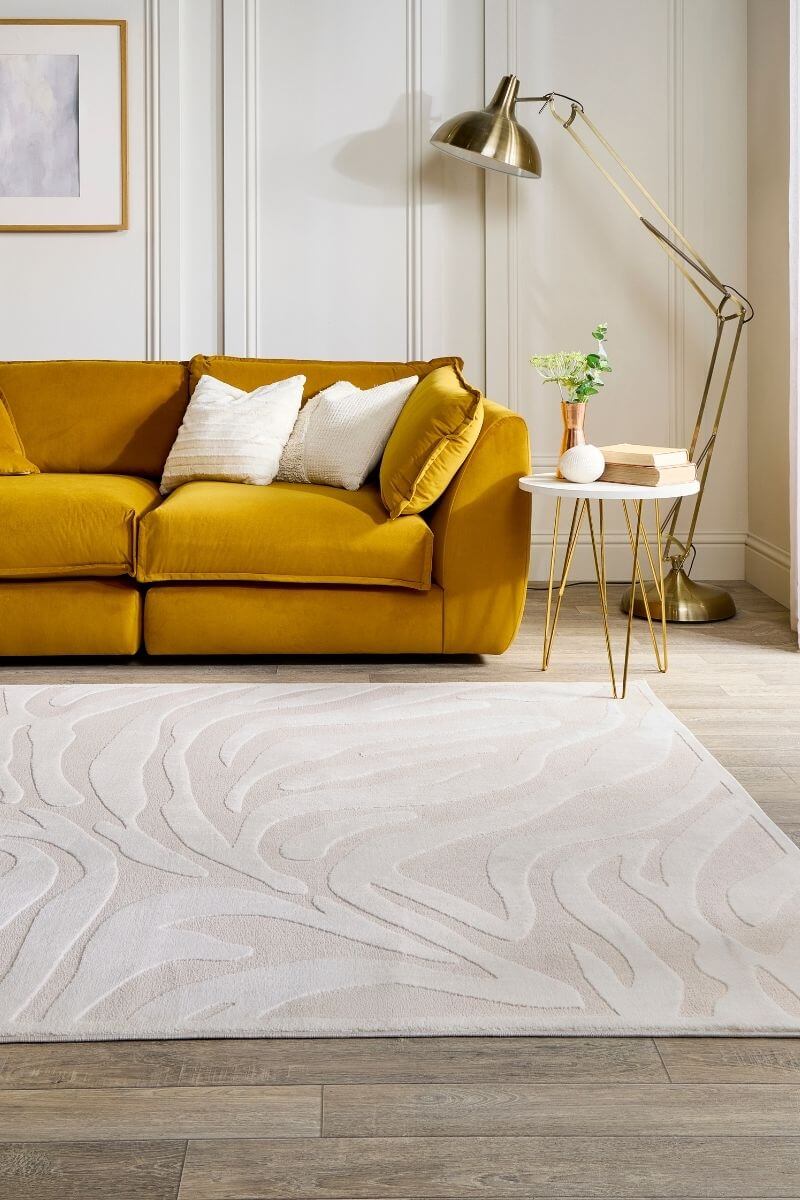 Yellow sofa in a living room with a white rug and gold lamp.