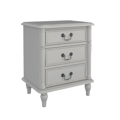 A left-hand corner angle view of a dove grey 3-drawer bedside chest with traditional design and metal handles next to a bed with additional accessories