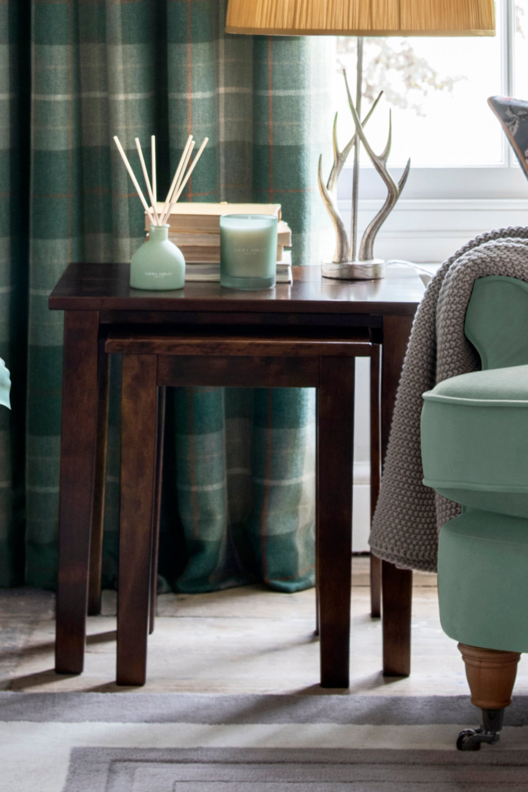 Wooden table with decorative items in a room with plaid curtains and a chair.