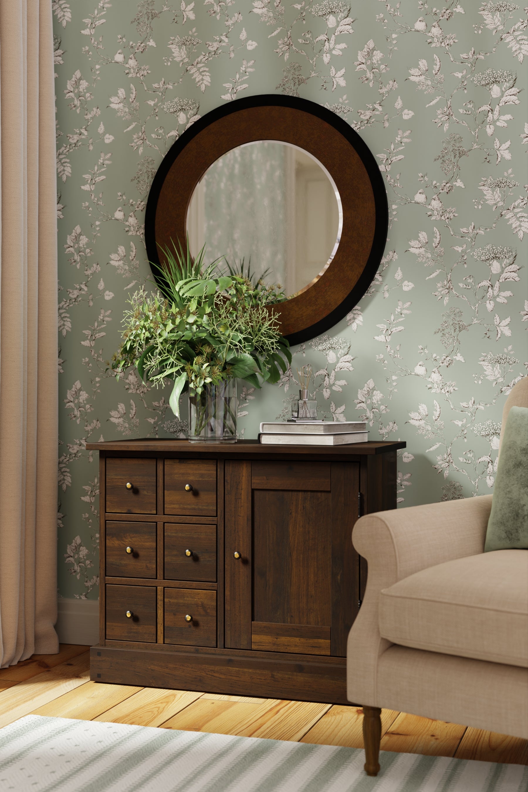 Round mirror above a wooden dresser with floral wallpaper and chair in the background.