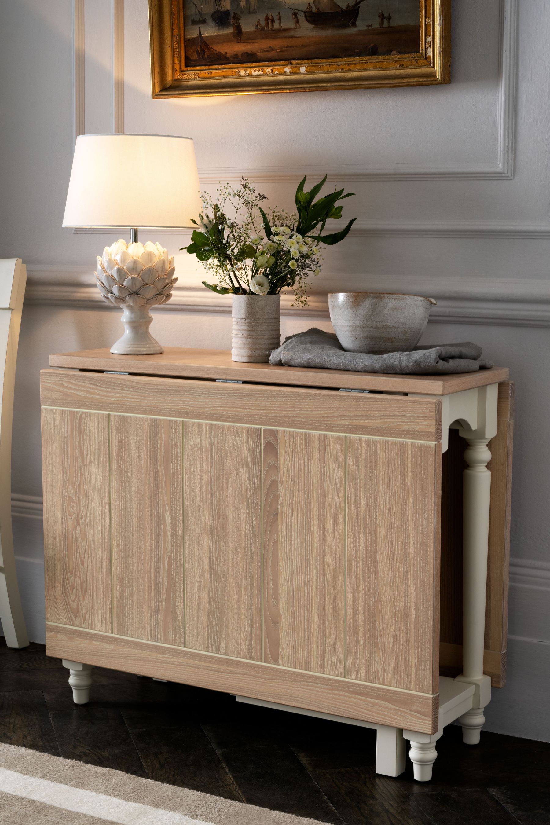 Wooden sideboard with lamp and flowers in a room with decorative wall molding.