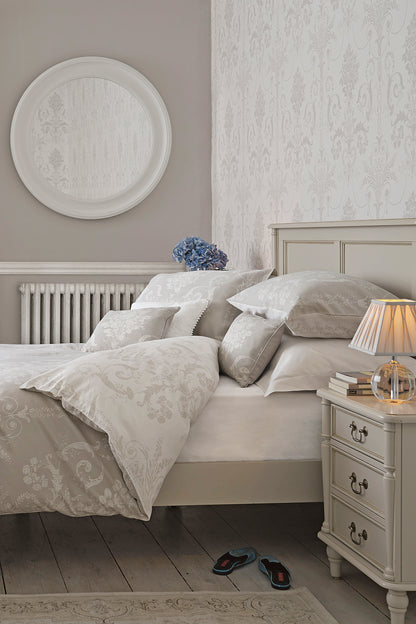 A right-hand angle of a Dove grey wooden bed frame with a headboard and footboard, with bedding and additional accessories.