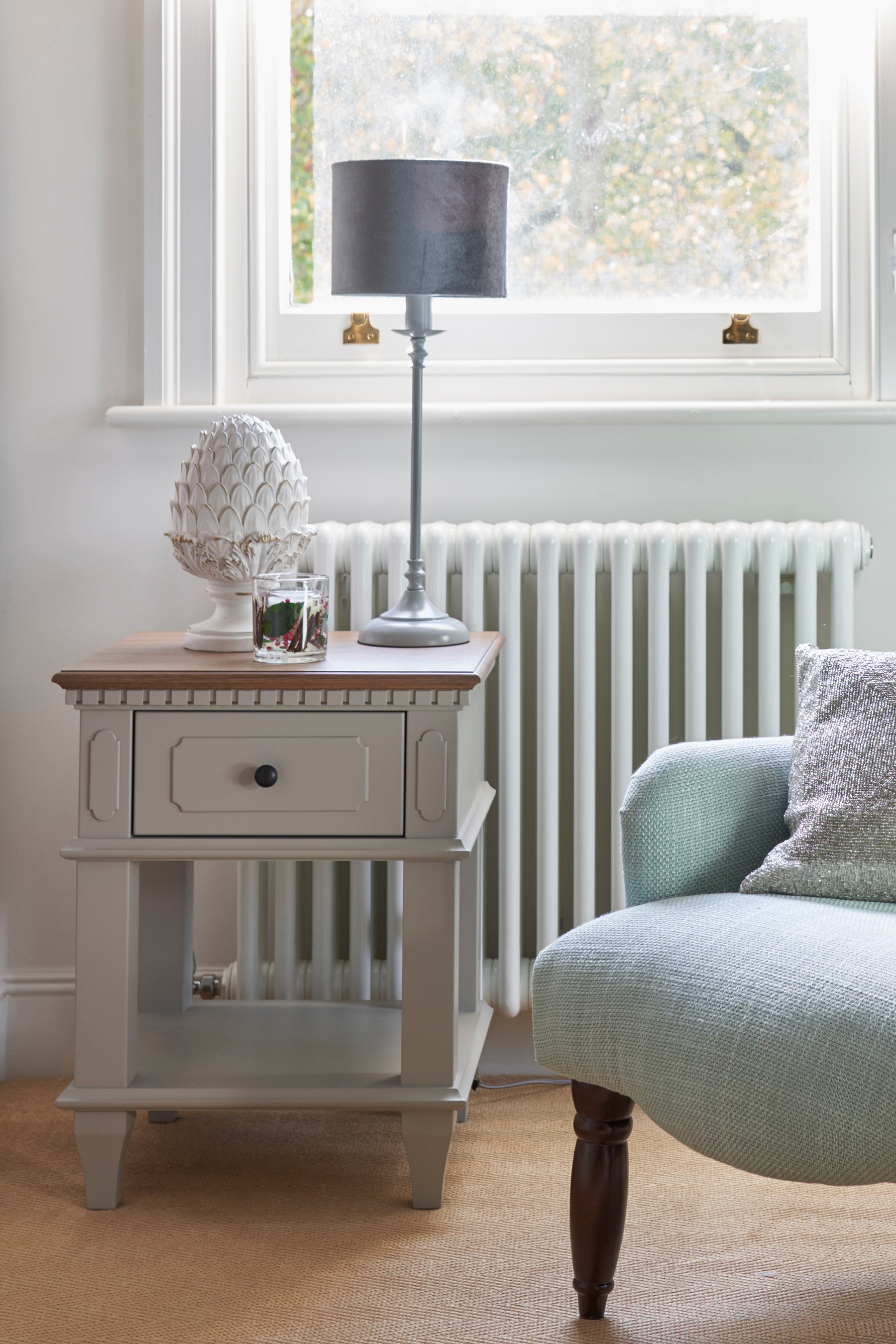Nest table with a lamp and decorative object next to a radiator and chair.