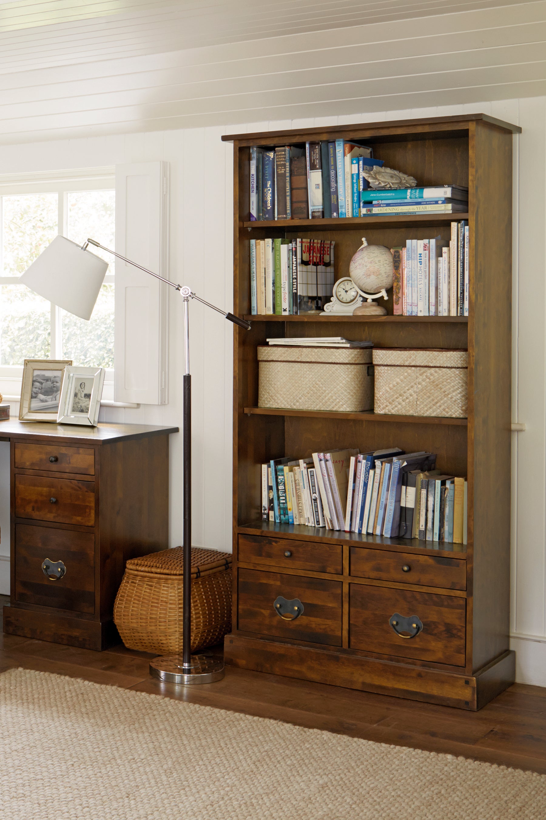 A dark chestnut wooden bookcase with four shelves and four drawers displaying books and decor in a room setting