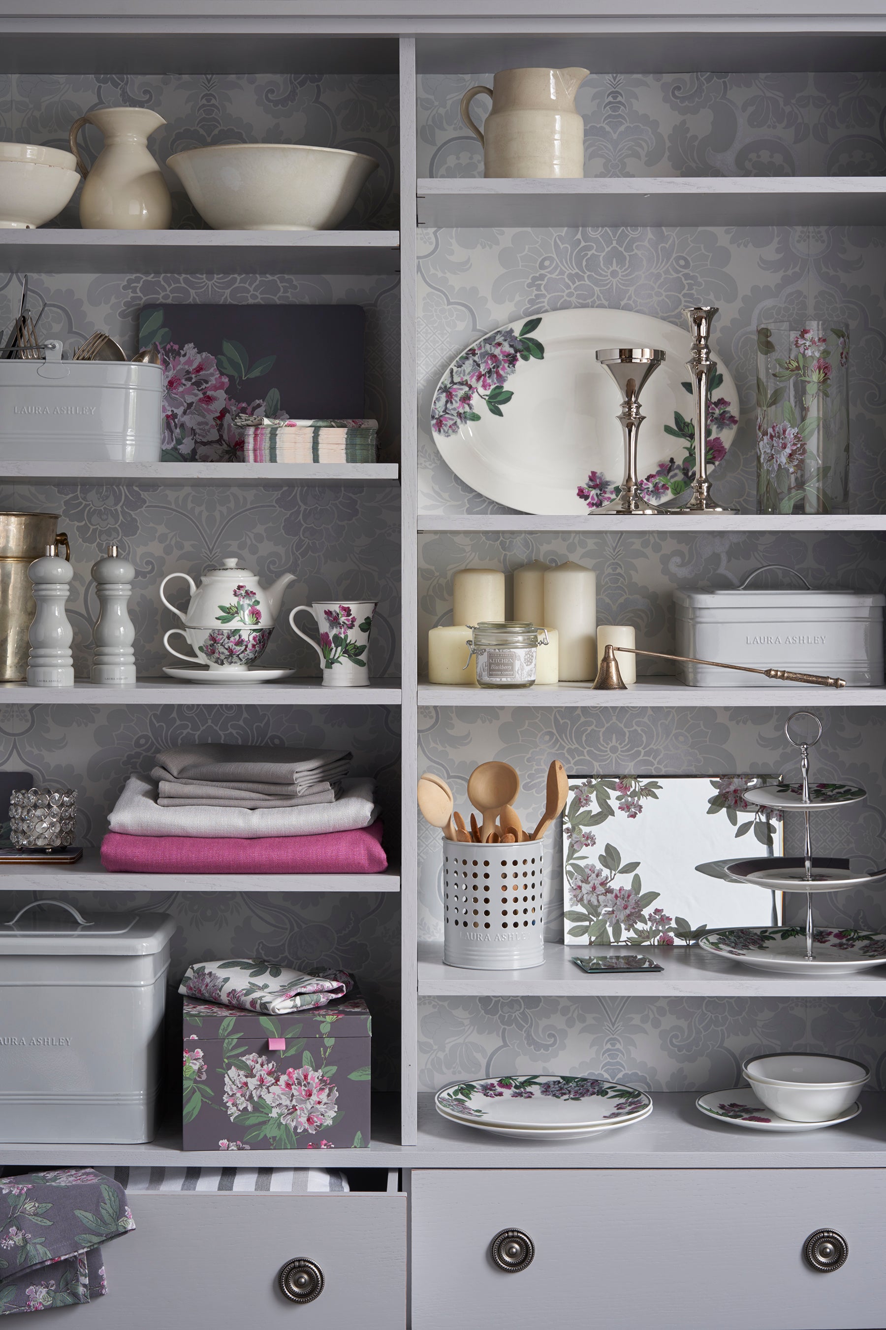 Grey bookcase with decorative items including plates, cups, and a teapot.