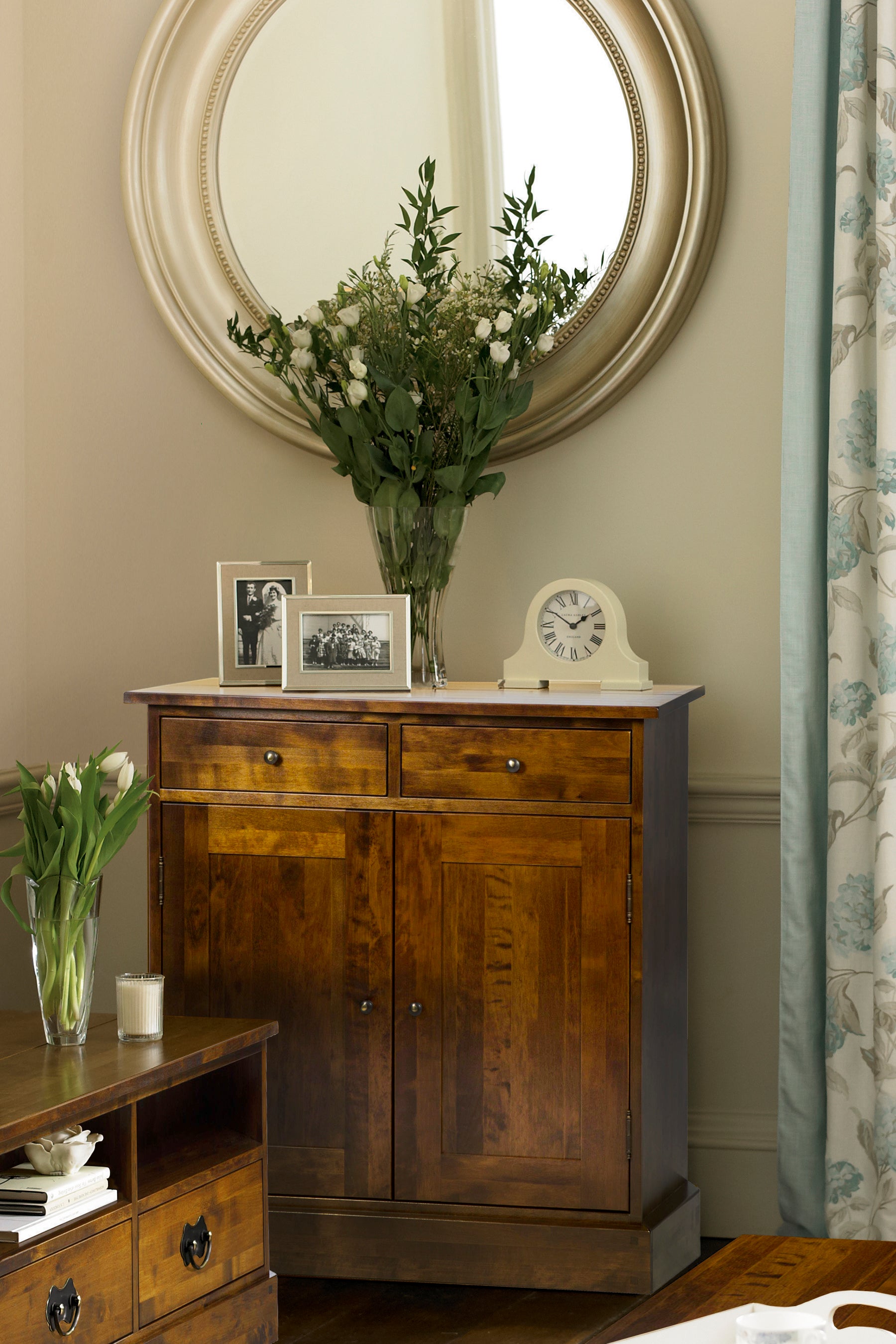 Wooden sideboard with vases, photos, and clock against a neutral wall.
